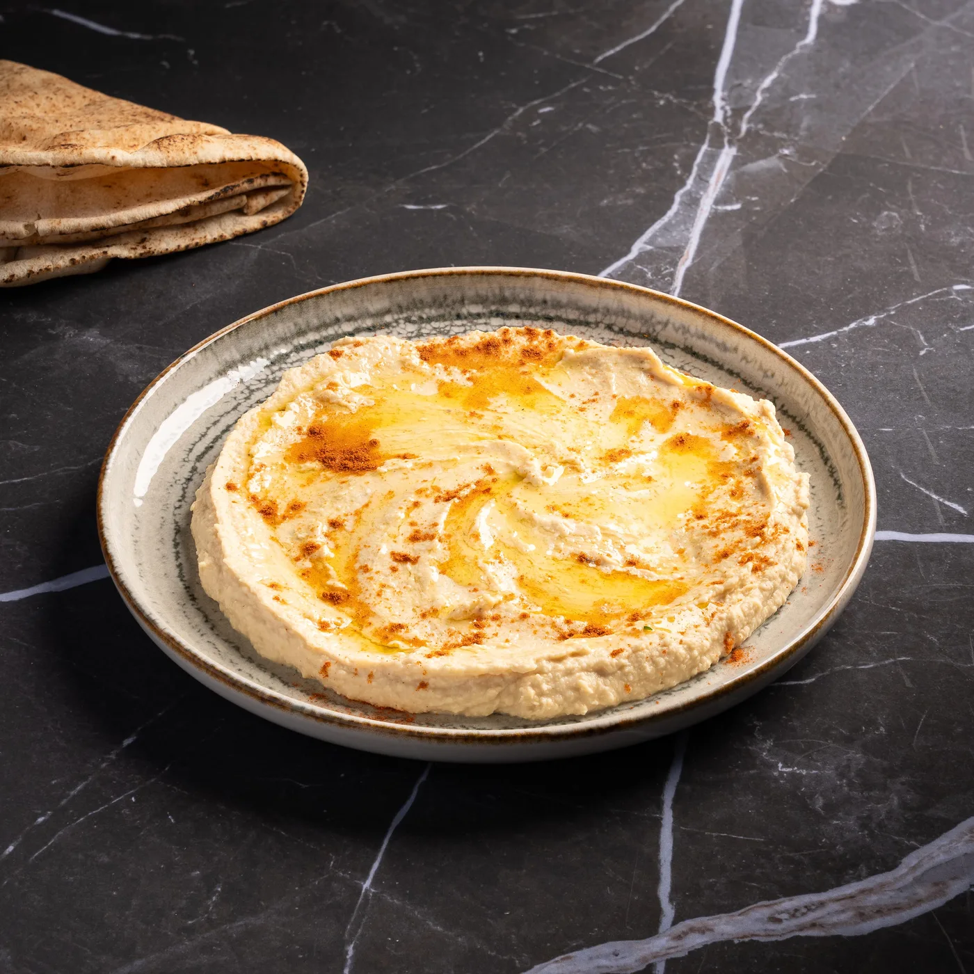 Hommos nature au paprika et filet d'huile d'olive, servi avec du pain libanais